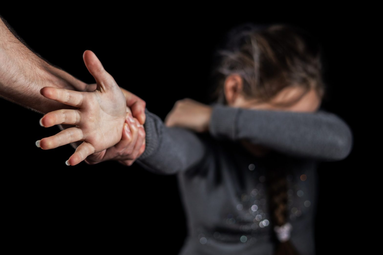 Enfant se cachant le visage avec une main d'homme la saisissant au poignet, illustrant une situation d'agression sur mineur