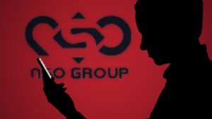 Silhouette d'un homme consultant son smartphone devant le logo NSO Group