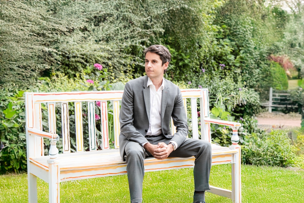 Gabriel Attal assis seul sur un banc dans un jardin