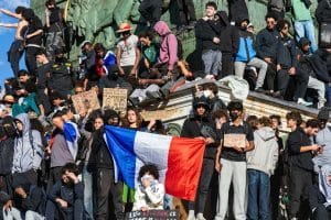 Foule de jeunes manifestants rassemblés sur un monument avec un drapeau français et des pancartes lors d'une mobilisation
