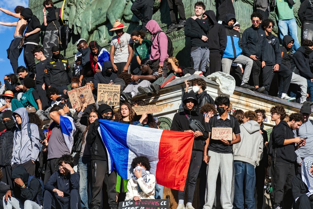 Foule de jeunes manifestants rassemblés sur un monument avec un drapeau français et des pancartes lors d'une mobilisation